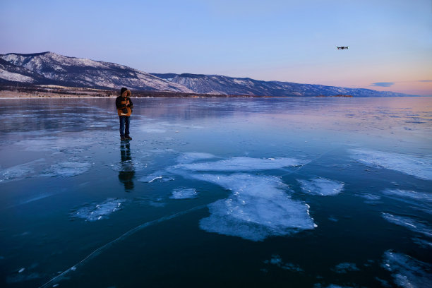 冰冻的贝加尔湖上美丽的日出，一名男子站在冰面上，操作无人机拍摄照片和视频图片下载