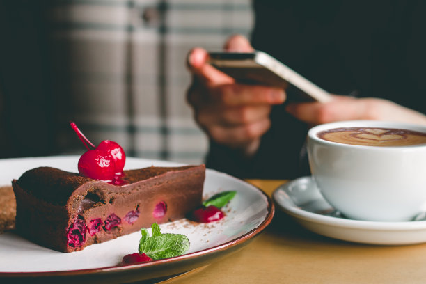 女孩拿着手机，咖啡和蛋糕在咖啡馆里。女性手拿着智能手机。女孩在咖啡馆聊天，查看社交媒体，或者用手机聊天图片下载