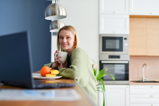 年轻女子在家里的厨房里用笔记本电脑图片下载