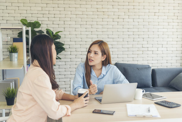 两个商业女性团队会议使用笔记本电脑在公司的办公桌。两名年轻女性，自由职业，阅读财务图表，计划分析市场数据。亚洲人团队办公公司。图片下载