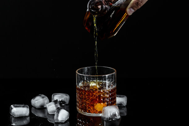 将威士忌冷冻倒入玻璃杯中。黑色底色的干邑或白兰地酒杯图片下载