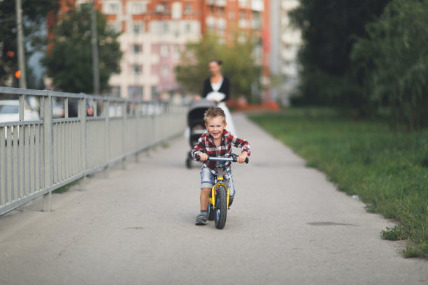 一位母亲推着婴儿车带着婴儿，儿子骑着平衡自行车在城市里散步，一位母亲带着兄弟姐妹。孩子骑平衡自行车图片下载