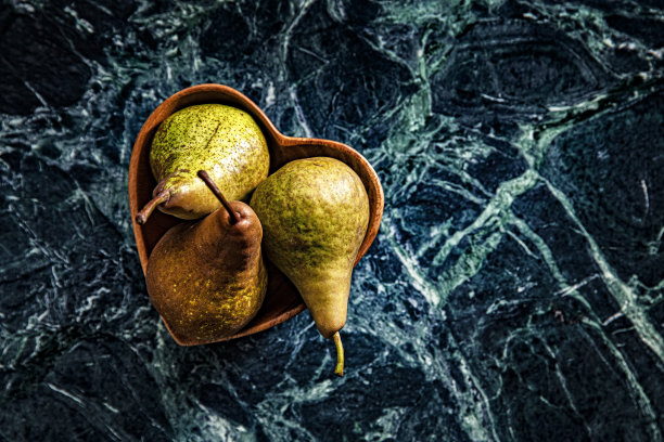 这是一张忧郁的照片，三个梨在一个心碗里，大理石绿色的背景图片下载