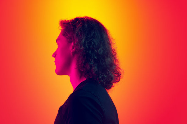 背面严肃的男人与长卷发摆孤立的梯度黄品红背景在霓虹灯。美、时尚、青春文化和情感的概念图片下载