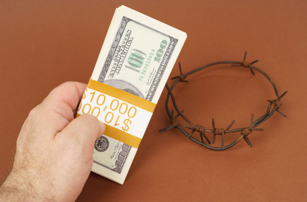 在一个棕色的平面上，一个男人手里拿着一捆美元，背景是铁丝网。图片下载