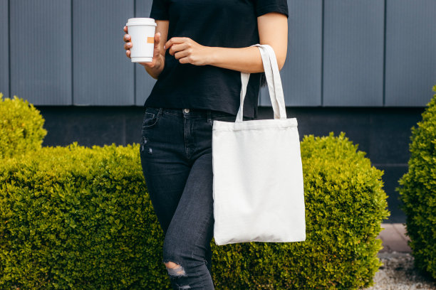 年轻的模特女孩在街上拿着白色的环保袋和咖啡杯，模仿图片下载