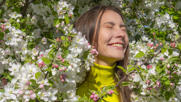 在一个阳光明媚的日子里，美丽的年轻女子在苹果树盛开的公园里的肖像。微笑的女孩与苹果树花。图片下载