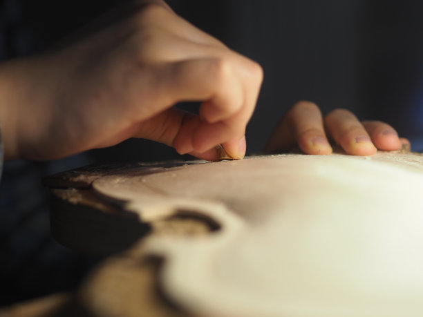 女制琴师在昏暗的灯光下用拇指平面雕刻小提琴板图片下载