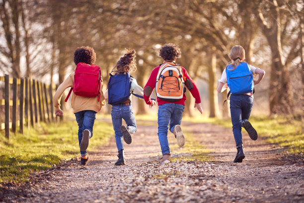 背着学校书包的孩子们在户外沿着乡间小路奔跑的背影图片下载