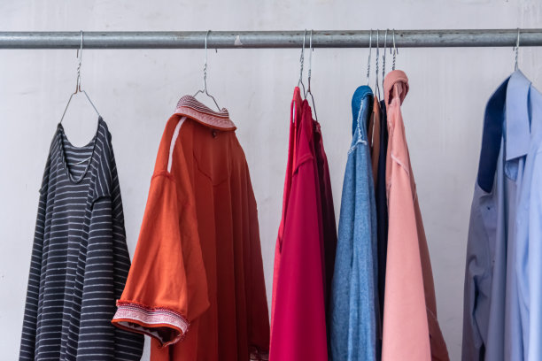 用银色衣架晾衣服在白色墙面背景的铁管上图片下载