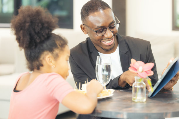 在一家咖啡馆，一对父女使用平板电脑，黑人企业家使用笔记本电脑。图片下载