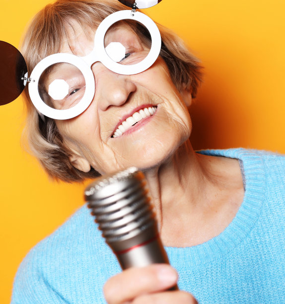 快乐的老妇人与大眼镜拿着麦克风和唱歌孤立的黄色背景图片下载