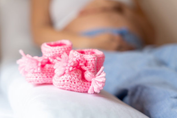 怀孕宝宝鞋子。怀孕的母亲女孩为婴儿抱着小童鞋。概念产妇，怀孕，分娩。美丽的母亲等待婴儿。图片下载