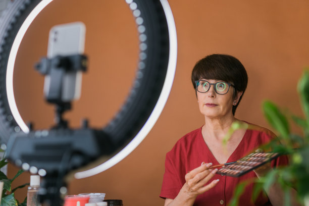 中年女性美妆博主或网红在家中使用环形灯和智能手机录制美妆产品视频图片下载