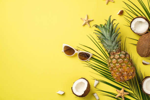 暑假的概念。顶视图照片的新鲜热带水果椰子菠萝太阳镜海星和棕榈叶孤立的黄色背景与copyspace图片下载
