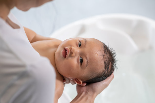 亚洲新生儿在浴缸中沐浴的喜悦。母亲用温水给儿子洗澡。快乐可爱的新生儿在浴缸微笑放松和舒适。新生儿护理理念图片下载