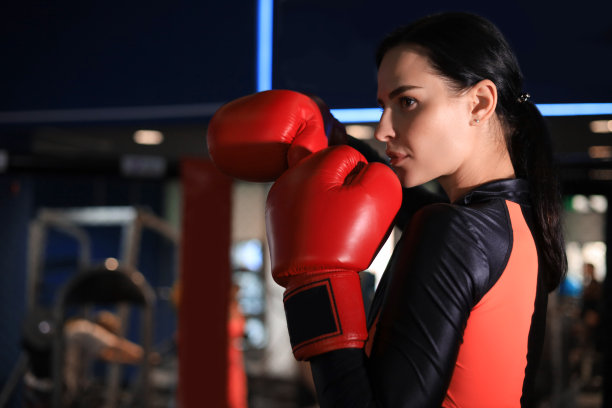 戴着红色拳击手套和运动服的女性站在拳击大厅的架子上。图片下载