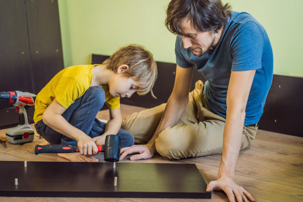 父子俩在组装家具。男孩在家帮他爸爸干活。幸福的家庭的概念图片下载