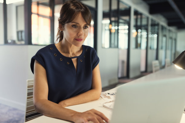 专注而迷人的女商人专注于她的笔记本电脑屏幕。现代办公背景图片下载