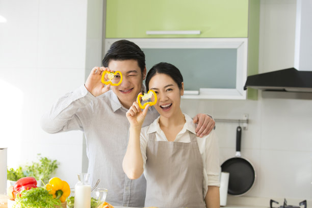 在家里的厨房里，小两口一起享受着烹饪的乐趣，就像拿着黄灯心椒片的照片图片下载