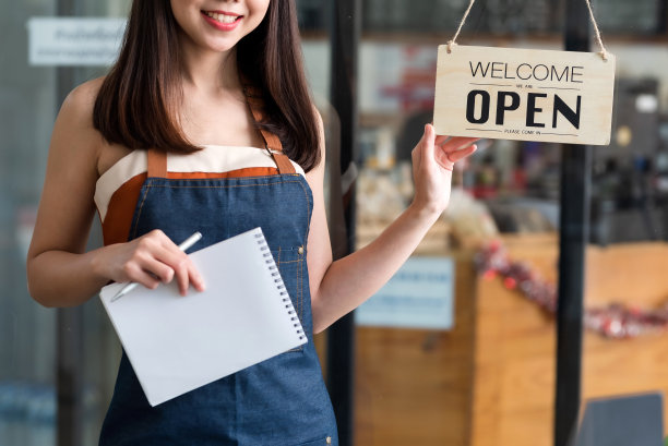 快乐的年轻企业主站着举着开放的招牌。图片下载
