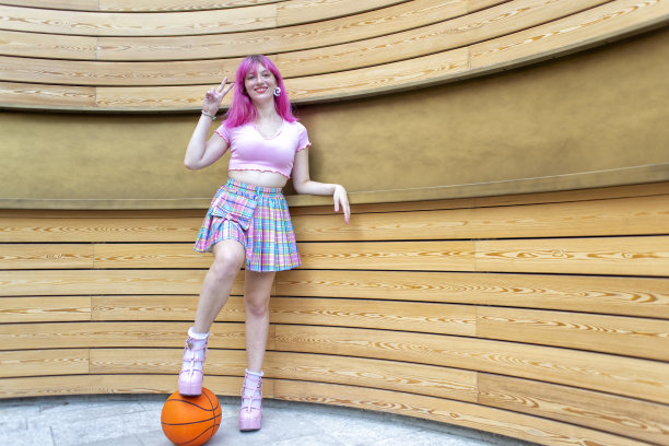 特写肖像另类的女人与粉红色的头发挂在寒冷和微笑站在现代木材背景墙孤立。快乐的女孩抱着篮球在户外。生活方式的概念图片下载