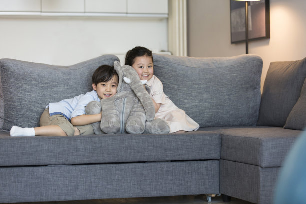 一个小女孩和一个小男孩在客厅的沙发上开心地玩着一个毛绒大象娃娃——照片图片下载