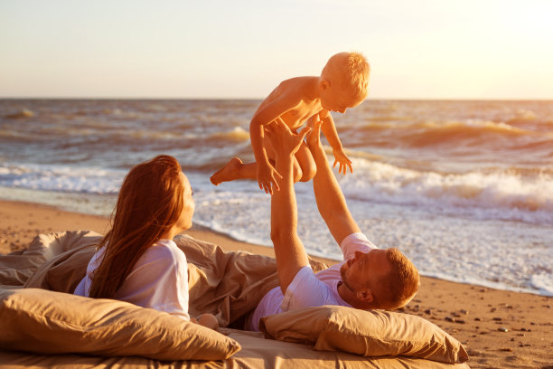 日落时分，爸爸把儿子抛向空中，躺在海边的床上图片下载