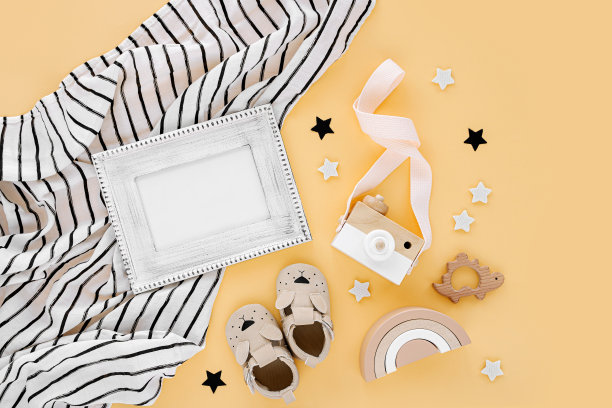 黑白细布襁褓与相框和婴儿拖鞋，玩具在黄色的背景。一套中性新生儿配件。平铺，俯视图图片下载