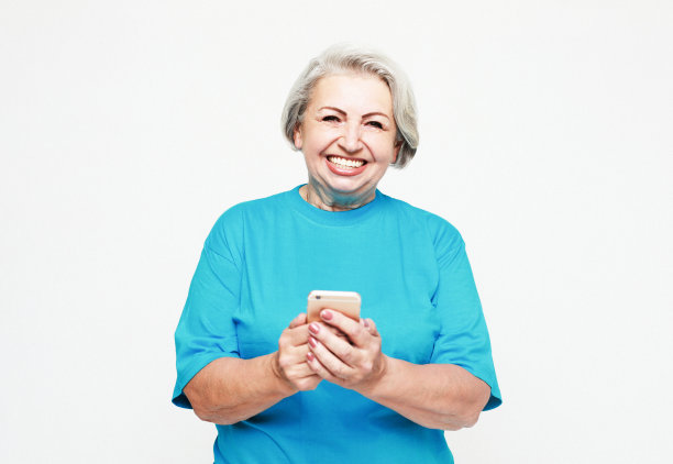 漂亮的高级女性穿着休闲服装，使用现代智能手机，站在白色背景上大声笑。图片下载