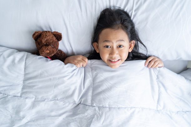 俯视图可爱的亚洲孩子小女孩醒来，躺在床上的玩具泰迪熊图片下载