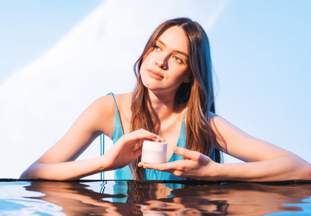 年轻美丽的女孩时尚模特的美丽肖像与健康的深色长发化妆品霜在手上的蓝色背景。用水拍美图片下载