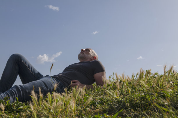 一个成年人的肖像躺在草地上，对着天空图片下载