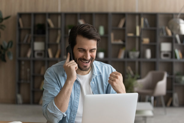 兴高采烈的商人坐在笔记本电脑旁，在手机上讨论完美的消息图片下载