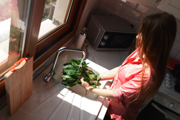 穿着围裙的年轻白人妇女在厨房里洗沙拉。有机健康家居饮食理念图片下载