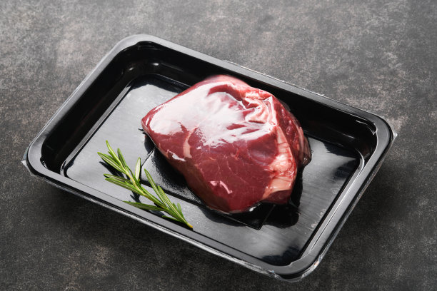 牛排。新鲜的生牛排，用叉子和迷迭香真空包装，黑色的石头背景。Vacoom包。前视图。设计理念的模型。图片下载