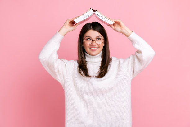 微笑的女孩用书本捂着头，用聪明的眼睛望着远方，梦想着未来的事业图片下载