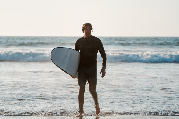 拉丁冲浪者在日落冲浪后带着冲浪板走出水面图片下载