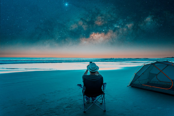 人们坐在星空下的海滩上，用智能手机拍摄银河图片下载