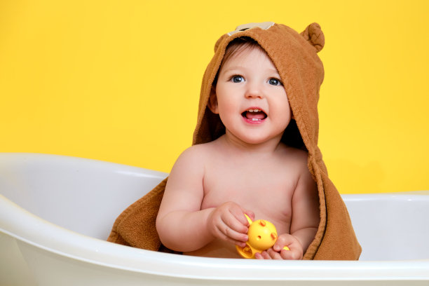 快乐的婴儿蹒跚学步的男孩在工作室黄色背景的白色浴缸里玩玩具。一岁的微笑的孩子图片下载