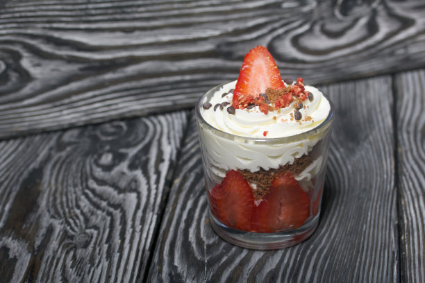 草莓加奶油的甜点。在玻璃罐里。在黑色的松木板上。特写镜头。图片下载