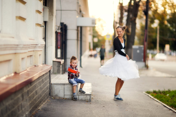 母亲和儿子在城市的人行道上，孩子在弹尤克里里，年轻的母亲在跳舞图片下载