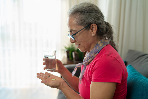 老妇人抱着药片和水坐在沙发上图片下载
