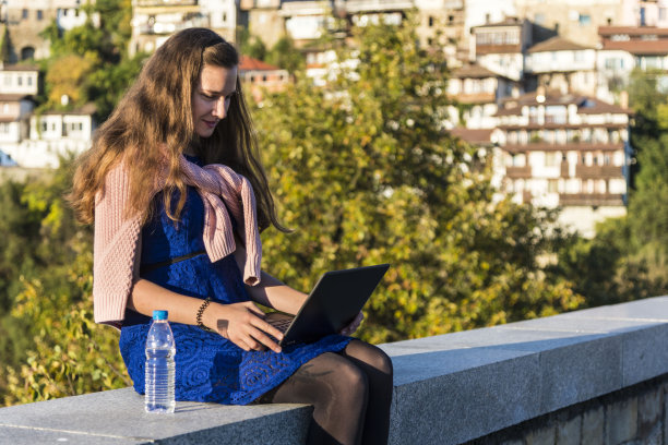 一个年轻女子在外面用笔记本电脑。图片下载