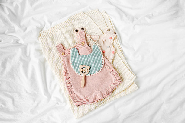 粉红色的紧身衣和围兜，在针织毛毯上。床上有一套小孩的衣服和配件。时尚的新生儿。平铺，俯视图图片下载
