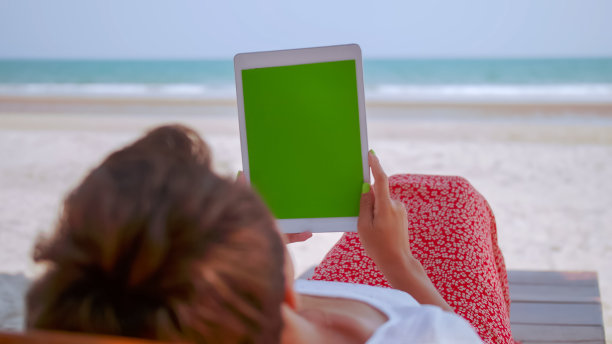 亚洲女性在沙滩上放松的时候正在平板电脑上看东西。图片下载