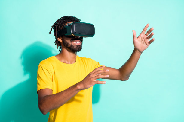 年轻快乐积极的好心情的照片男子使用vr眼镜穿着黄色t恤孤立在蓝绿色的背景图片下载