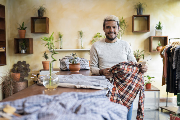 拉丁美洲男服装店工人靠在桌子上，手里拿着衬衫图片下载