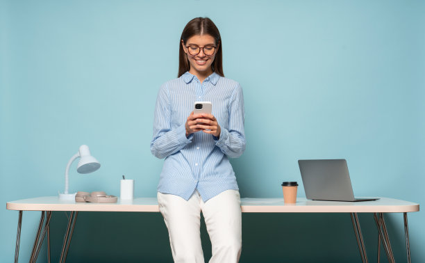 人力资源经理坐在蓝色工作室背景的桌子上，查看手机上的信息图片下载