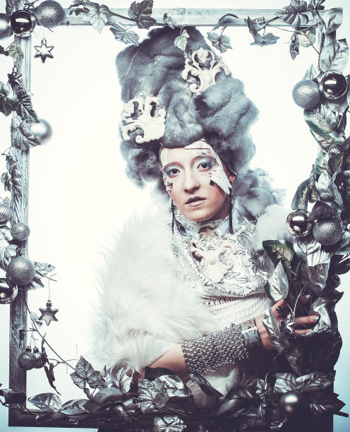 年轻女子与银色艺术化妆，假发，摆在一个装饰着圣诞装饰的银色框架。图片下载